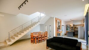 Een ruime woonkamer met trap, eettafel en zwarte bank.