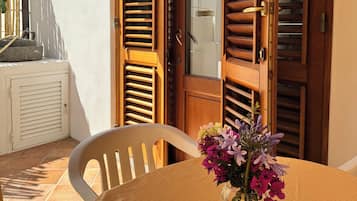 Une pièce avec une porte en bois, une chaise blanche, une table ornée d’un vase de fleurs et un sol carrelé.