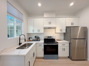 Una cocina moderna con gabinetes blancos, un refrigerador de acero inoxidable, un horno empotrado y un ventanal que proporciona luz natural.