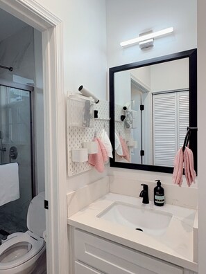 Un baño con inodoro, lavabo, espejo, toallero y zona de ducha.