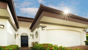 Une maison à deux étages avec un garage, un portail noir et un ciel ensoleillé.