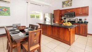Une cuisine avec des meubles de rangement en bois, un réfrigérateur, un four à micro-ondes et un panier de fruits posé sur le comptoir.
