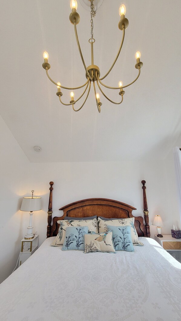 A bedroom with a wooden bed, a chandelier, bedside lamps, and patterned pillows.