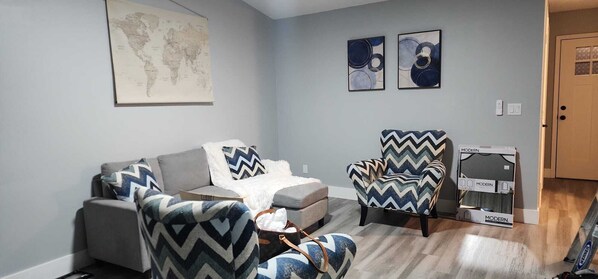 Una sala de estar con un sofá gris, dos sillones estampados, una mesita y un mapa mundial en la pared.