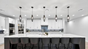 A modern kitchen with a large island, black bar stools, and pendant lighting. - Zion Canyon Mist Resort House (Hurricane)