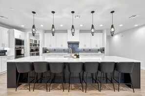 A modern kitchen with a large island, black bar stools, and pendant lighting. - Zion Canyon Mist Resort House (Hurricane)