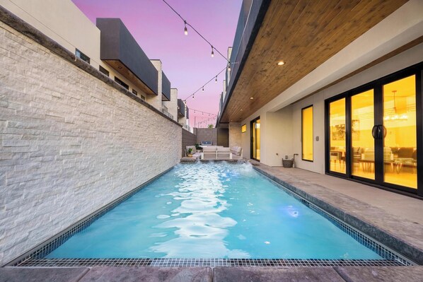 A swimming pool with a stone wall on one side and a wooden ceiling on the other, with string lights above.