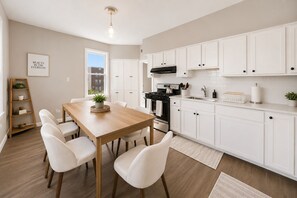 Une cuisine moderne avec des meubles blancs, une table à manger en bois et un poêle noir.