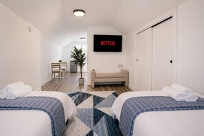 Et hotelværelse med to senge, en sofa, et TV ophængt på væggen, et lille bord med stole og en potteplante.
