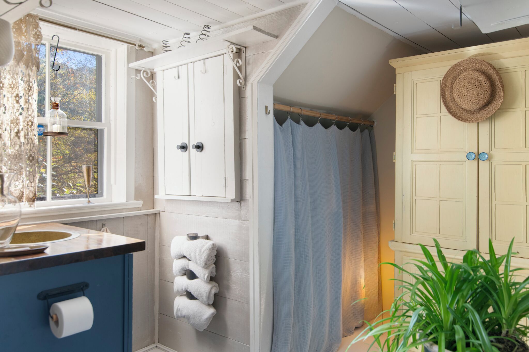 A bathroom with a white vanity, a towel rack, a hanging glass jar, and a blue shower curtain.