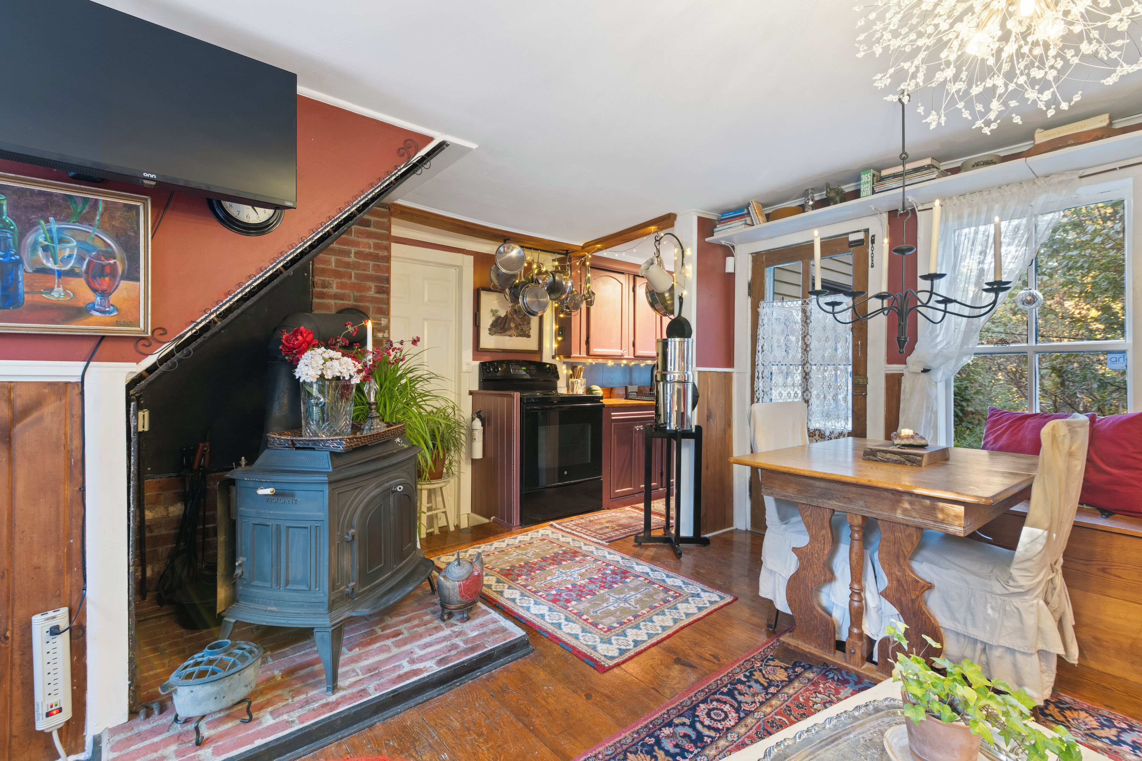Une cuisine chaleureuse avec un escalier en bois, un coin repas avec une table et des chaises, et une vue sur l’extérieur par une fenêtre.