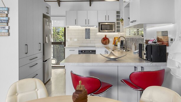 A modern kitchen with white cabinets, a microwave, a sink, and a dining area with red chairs. - Family-Friendly 3BR Home Close to Lake Taupō (Taupō)