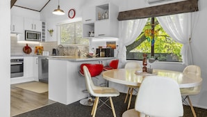 A modern kitchen with white cabinetry, a central island, and a dining area with white and red chairs. - Family-Friendly 3BR Home Close to Lake Taupō (Taupō)