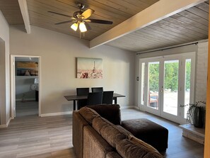 A spacious living area with a ceiling fan, a dining table with chairs, a sofa, and a large window with a view of greenery. - 2-bedroom house in charming Rancho Mirage with AC (Rancho Mirage)