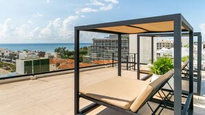 Eine Dachterrasse mit Liegestuhl, einer Pergola und Blick auf Stadt und Meer.