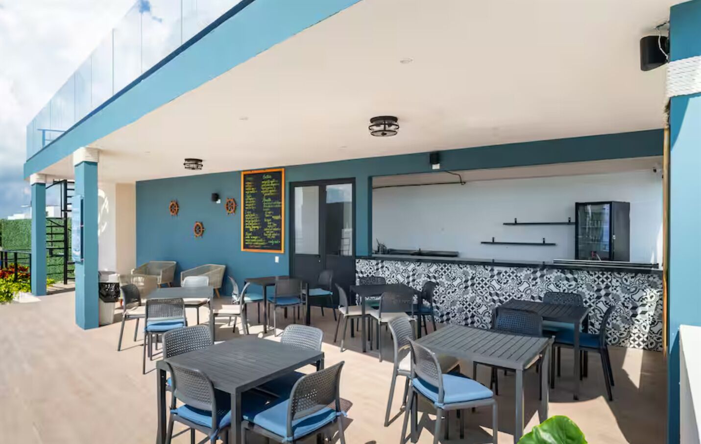An outdoor patio area with tables and chairs, a bar counter, and a menu board.