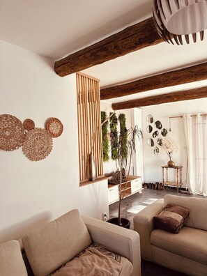 A living room with a sofa, a wooden beam ceiling, a wall with woven decorations, and a potted plant.