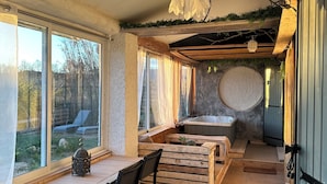 A room with a wooden table, chairs, a bench, a bathtub, and a view of the outdoors.