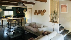 A living room with a sofa, a coffee table, and a hanging plant. There is a kitchen in the background.