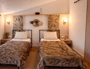 A room with two beds, each with a headboard, a wall-mounted shelf with decorative items, and wall sconces.
