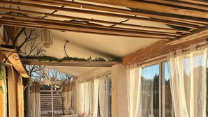 A cozy room with a wooden bench, a sofa, a small table with a plant, and a window with sheer curtains.