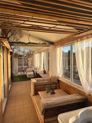 A cozy room with a wooden bench, a sofa, a small table with a plant, and a window with sheer curtains.