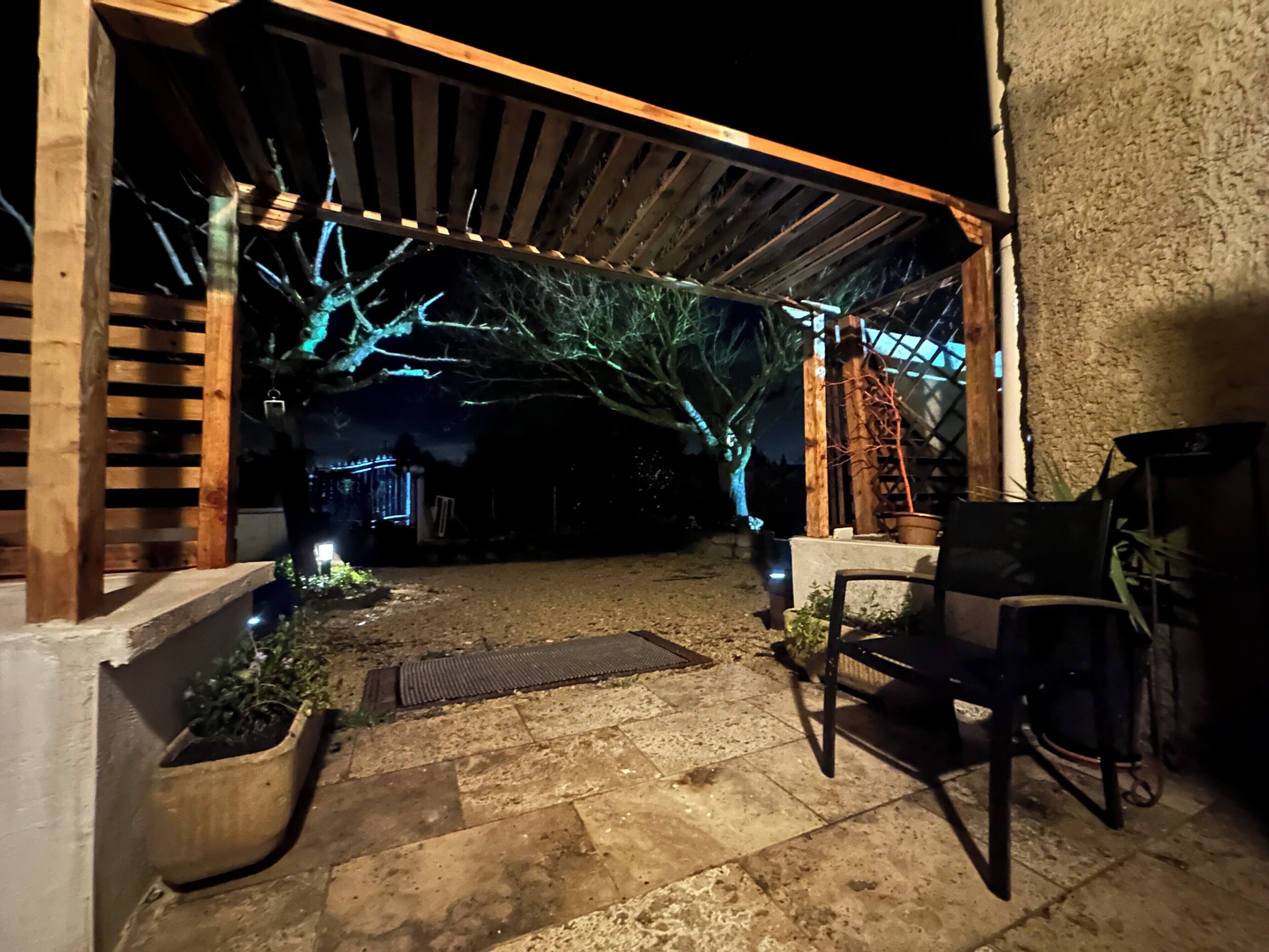 A covered outdoor area with a wooden pergola, potted plants, and a seating area.