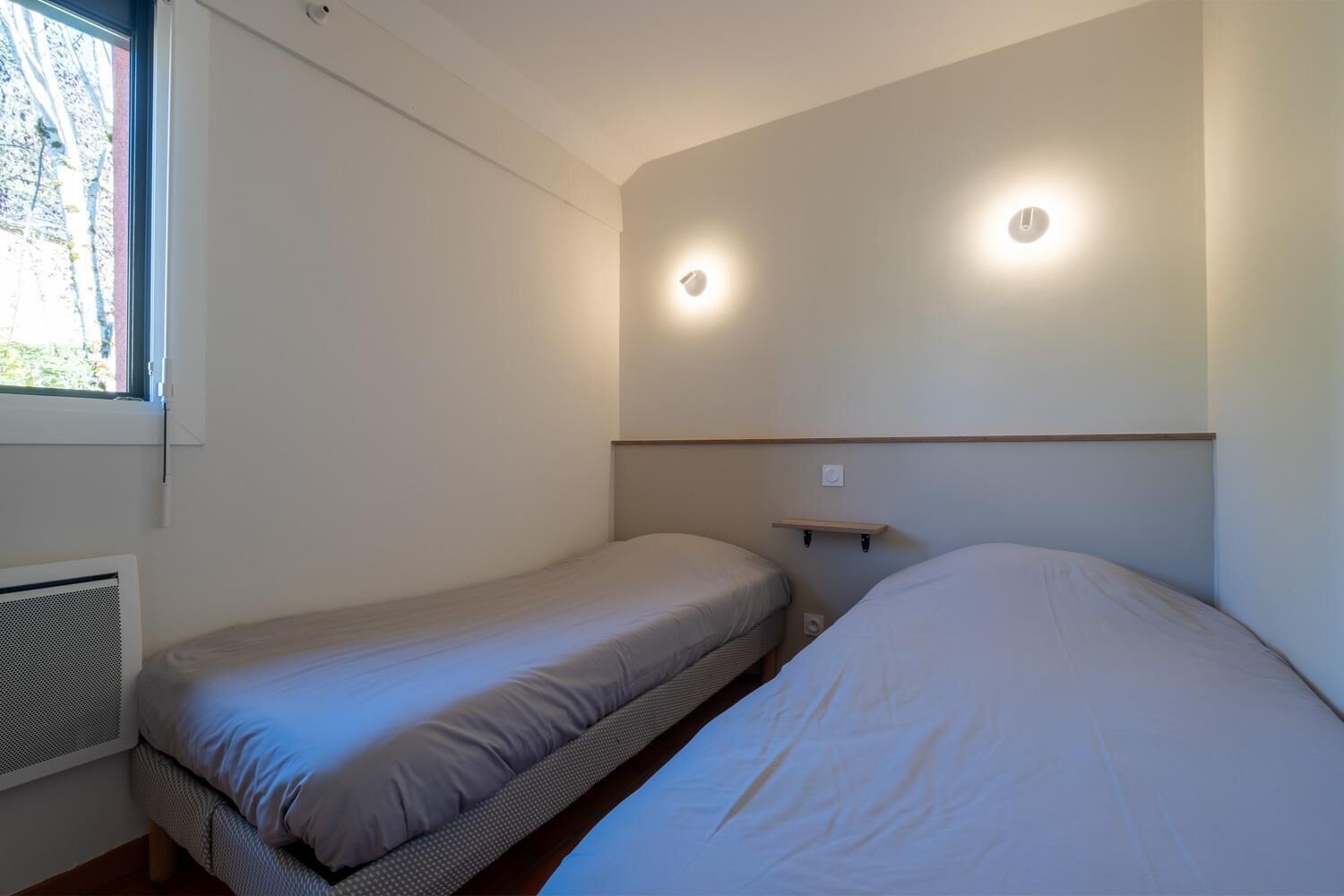 Una habitació petita, amb espai per a dues persones, una finestra i llums integrades a la paret.