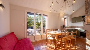 A dining area with a table set for four, a red sofa, and a kitchen in the background. - Gite 6/8 pers. PREMIUM - Village des Bruguières (LA CANOURGUE)