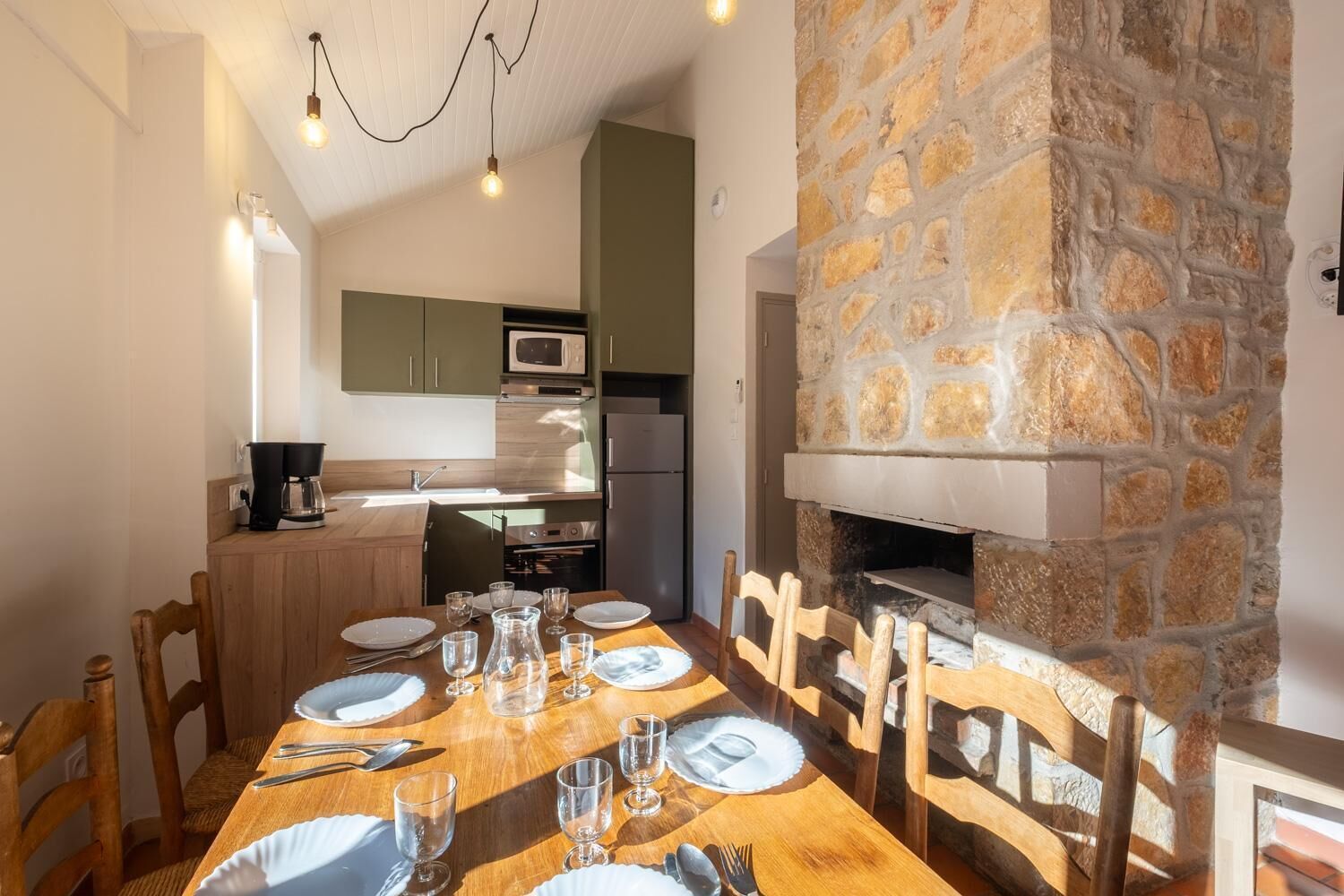 Un coin repas agrémenté d’une cheminée en pierre, d’une table en bois et de chaises.
