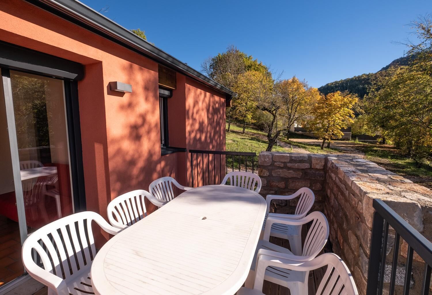 Une terrasse avec une table et des chaises, un mur en pierre et une vue sur les arbres et les collines.
