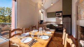 A dining area with a wooden table set for four, kitchen appliances, and a stone fireplace. - Gite 6/8 pers. PREMIUM - Village des Bruguières (LA CANOURGUE)