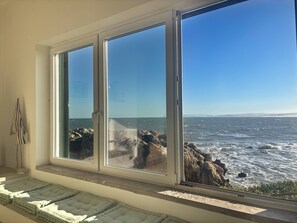 A room with a large window overlooking a rocky coastline. - Baleal Oceanfront: Terrace & Sunrise Sea View (Peniche)