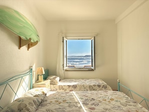 A bedroom with two beds, a window with a view of the sea, and a green curtain. - Baleal Oceanfront: Terrace & Sunrise Sea View (Peniche)