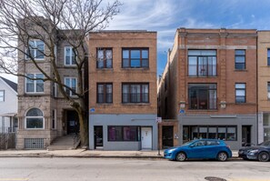 A street view with two-story brick buildings, a tree, and parked cars.