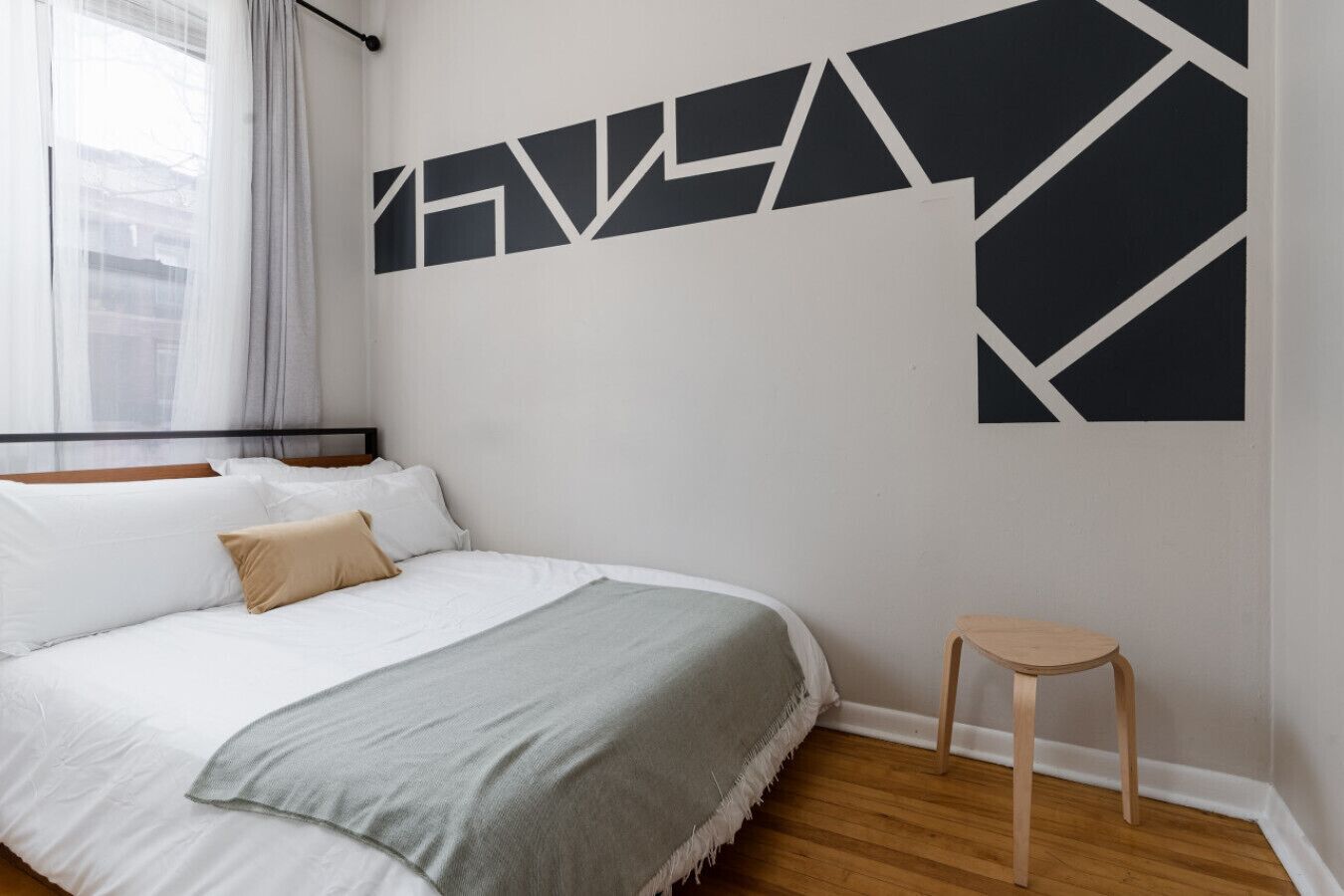 Une chambre à coucher comprenant un lit, une table de chevet et une œuvre d’art murale aux motifs géométriques.