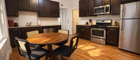 A modern kitchen with dark wooden cabinets, stainless steel appliances, and a round wooden dining table with chairs.