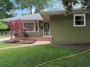 A green house with a porch, a small tree, and a visible number 5012.