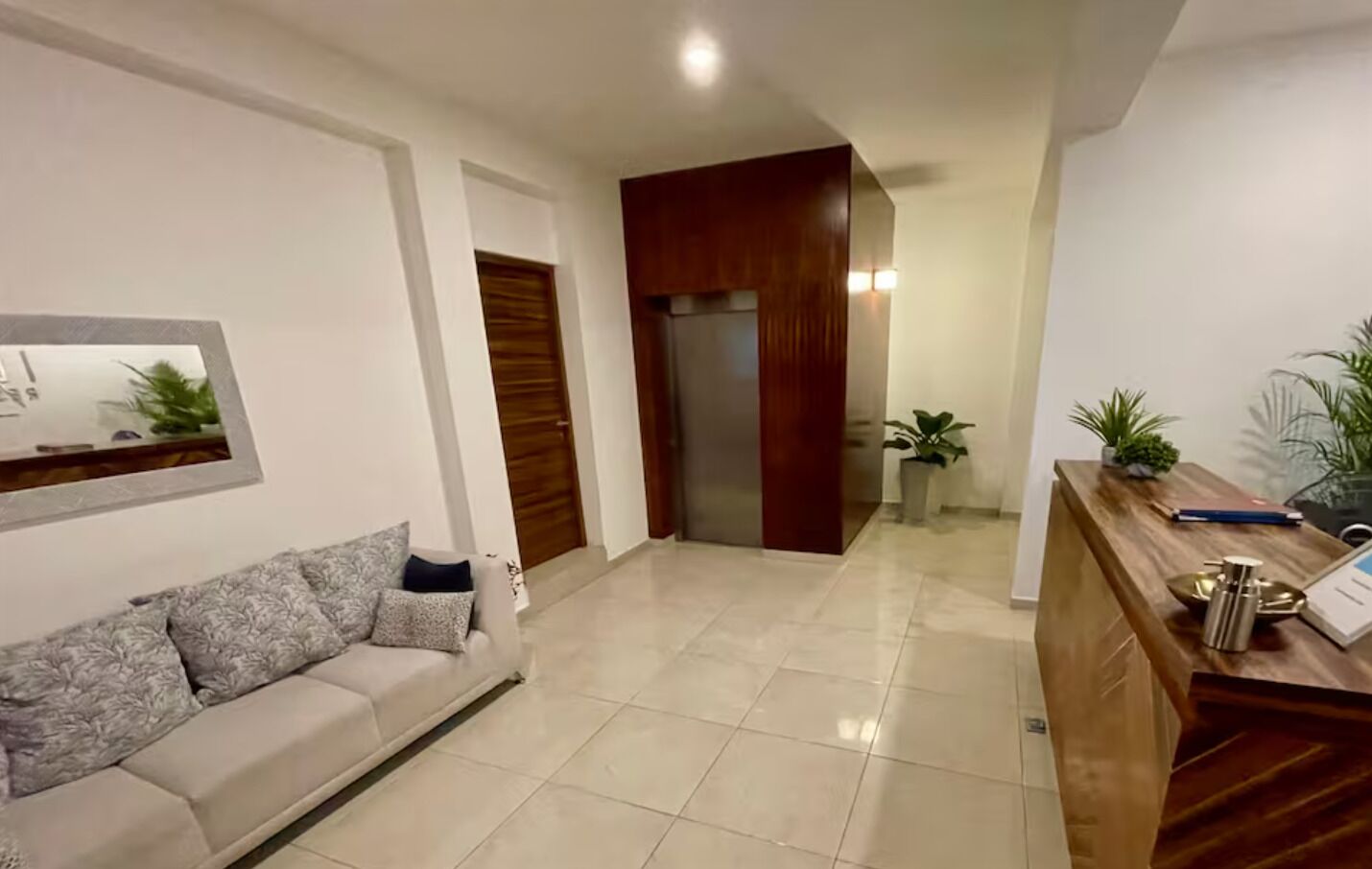 Un salon moderne avec un canapé, un comptoir d’accueil en bois et une porte donnant sur une autre pièce.