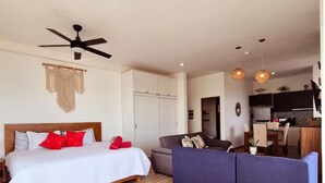 Een slaapkamer met een bed, een plafondventilator en een kitchenette op de achtergrond.
