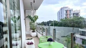 Een balkon met glazen hekwerk, plantenbakken, een groene tafel en een hangende lamp.