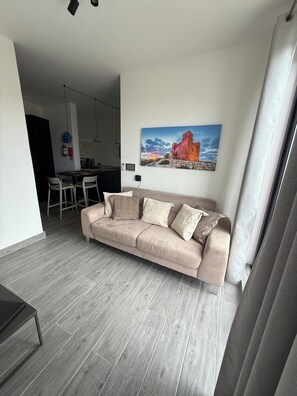 A modern living room with a beige sofa, a dining area with a table and chairs, and a painting of a castle on the wall. - Doni Signature Penthouse with HotTub and Sea Views (Il-Mellieħa)