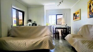 Ein Zimmer mit zwei Betten, einem Esstisch, Stühlen, einem Fenster und einem Bild an der Wand.