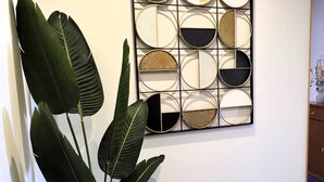 Et vægmonteret abstrakt kunstværk med geometriske former og en potteplante i forgrunden.