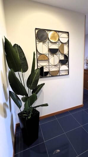 Une œuvre d’art abstraite fixée au mur, composée de formes géométriques, avec une plante en pot placée au premier plan.