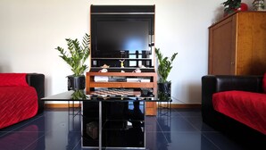 En stue med et fladskærms-TV, et glas sofabord, to røde sofaer, et træskab og to potteplanter.