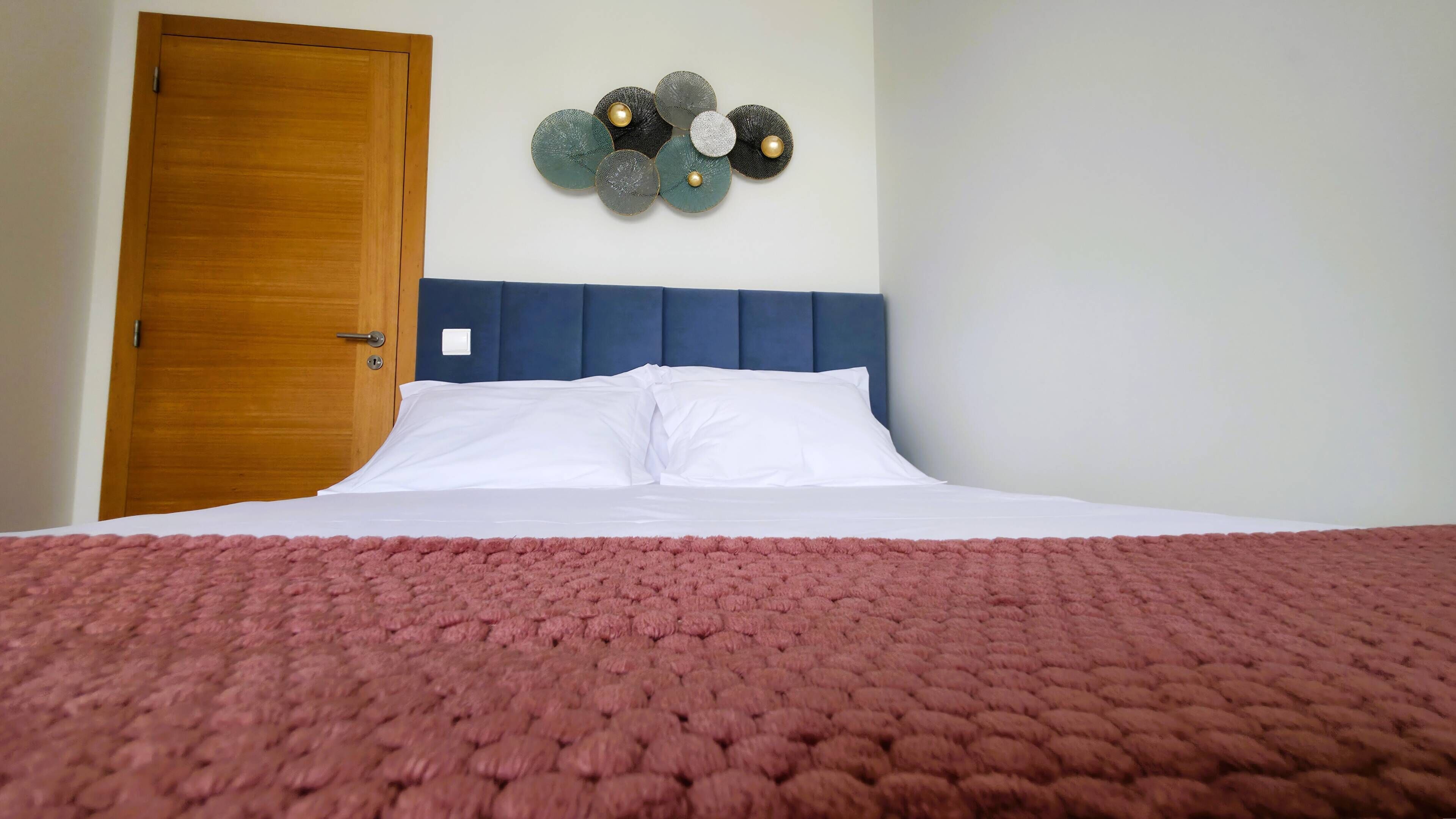 Ein Bett mit weißen Leinen, einem blauen Kopfteil und einer rosa, strukturierten Decke.