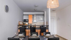 Uma área de refeições com uma mesa posta para quatro pessoas, cozinha ao fundo e um lustre.