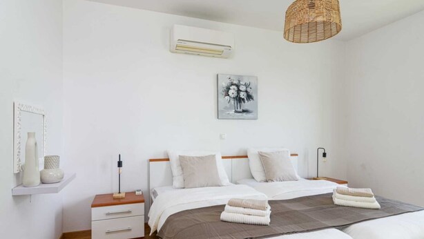 Um quarto com cama, mesas de cabeceira, um ar condicionado fixado na parede, luminária pendente e uma obra de arte emoldurada.