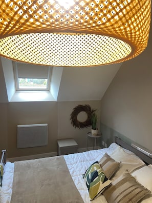 Une chambre à coucher avec un lit, une petite table de chevet ornée d’une plante, un radiateur et une fenêtre donnant sur un beau paysage.